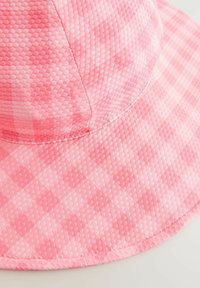 Chapeau seau rose présente un motif texturé en damier avec un bord légèrement courbé et des bords cousus, fabriqué à partir d'un tissu léger.