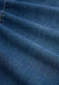 Dżinsowy materiał w ciemnoniebieskim odcieniu o gładkiej fakturze, z delikatnym diagonalnym splotem i widocznymi liniami ściegów.