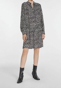 Abito a righe bianche e nere con maniche lunghe, collo a camicia e vita cin cin. Indossato con stivali neri alla caviglia. Tessuto morbido.