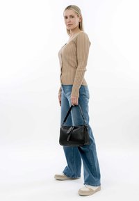 Black leather handbag with zip closure and short strap, paired with a ribbed beige long-sleeve top and light blue jeans.