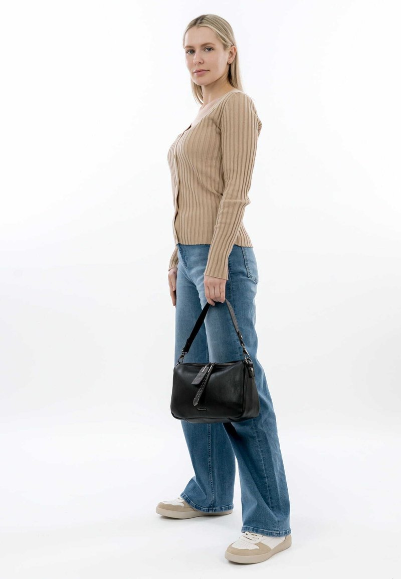 Black leather handbag with zip closure and short strap, paired with a ribbed beige long-sleeve top and light blue jeans.
