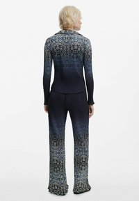 Tailliertes zweiteiliges Outfit mit floralem Muster, bestehend aus langärmeliger Bluse und ausgestellten Hosen, in Dunkelblau, das zu helleren Tönen übergeht.