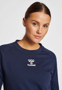 Sweatshirt bleu marine en tissu doux, avec un col rond et des manches raglan. Un logo blanc est imprimé sur la poitrine.