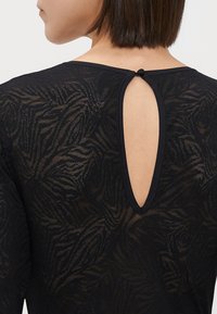 Melnas mežģīņu blūze ar lapu rakstu, apaļu kakla izgriezumu un atslēgvārda izgriezumu aizmugurē, kuru aizver maza pogas detaļa.