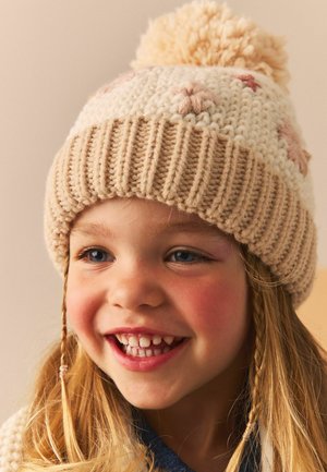 Strickmütze für den Winter in Creme und Beige mit einem großen Pompon oben, verziert mit rosa Sternmustern und Ohrenklappen. Ideal für kaltes Wetter.