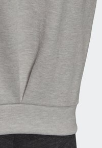 Tissu gris clair avec une couture et un détail froncé ou plissé près de l'ourlet inférieur au-dessus d'un tissu texturé plus foncé.