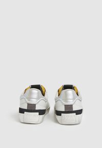 Sneaker argento e bianche con una tomaia in pelle testurizzata, accenti neri e grigi, e l'anno "1973" impresso sul tallone posteriore.