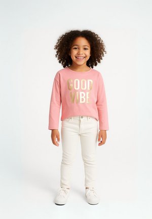 Ljusrosa långärmad sweatshirt med "GOOD VIBE" i metallisk guldtext, ihop med vita slim-fit jeans och vita sneakers.
