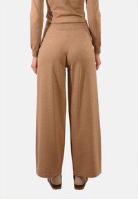 Pantaloni a gamba larga in un morbido tessuto color marrone chiaro con una leggera lucentezza. Presentano una vita elasticizzata e una vestibilità ampia, che si estende fino alle caviglie.