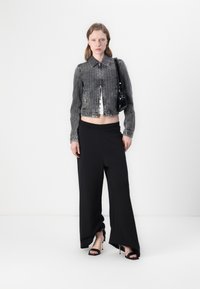 Giacca di jeans grigia corta con chiusura a bottoni, abbinata a pantaloni neri a gamba larga con cintura elastica e sandali neri con tacco.