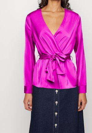 Top avvolgente in satin rosa con maniche lunghe e dettaglio a fiocco in vita, abbinato a una gonna di denim con bottoni frontali.