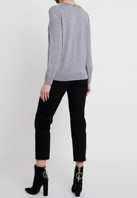 Harmaa pitkähihainen neule pyöreällä kaula-aukolla, yhdistetty mustiin slim fit -housuihin. Mallilla on päällä mustat avokkaat, joissa on vetoketjuyksityiskohta.