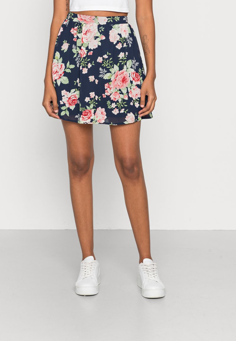 Saia floral com fundo azul-marinho, rosas cor-de-rosa e folhas verdes. Feita de tecido leve, com forma evasê e cintura elástica.