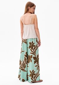 Beige mouwloos topje met verstelbare bandjes, gecombineerd met wijde pijpenbroeken met een teal achtergrond en een groot bruin bloemmotief.