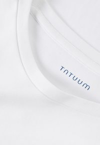 Biely bavlnený tričko s okrúhlym výstrihom. Obsahuje plochý golier a potlačenú etiketu s nápisom "TNTUUM" v modrej farbe na vnútornej strane krku.