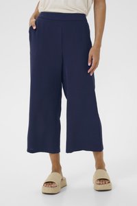 Pantalons large en marine avec un tissu texturé, une taille haute et des poches latérales. Associés à des espadrilles de couleur naturelle.