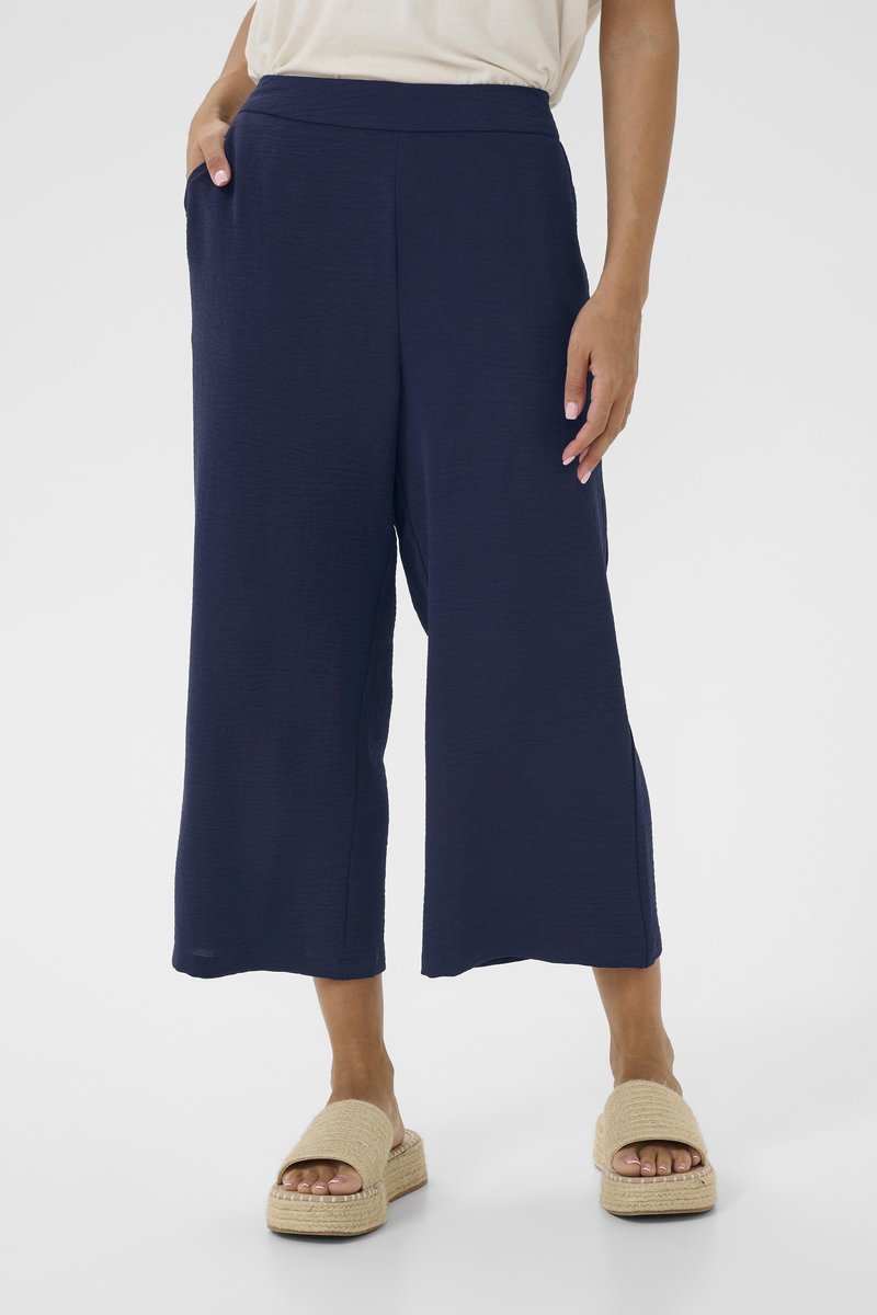 Pantalons large en marine avec un tissu texturé, une taille haute et des poches latérales. Associés à des espadrilles de couleur naturelle.