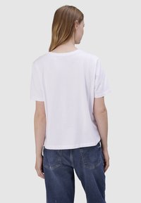 T-shirt en coton blanc avec un col rond et des manches courtes, à coupe décontractée et ourlet droit, porté avec un pantalon en denim bleu.