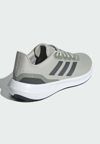 Svetlo šedá športová obuv s textúrovaným zvrškom, tromi čiernymi prúžkami a bielou podrážkou s šedým akcentom na päte.