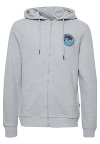 Haut à fermeture éclair gris avec une poche kangourou, un capuche à cordon et un accent de logo circulaire sur la poitrine gauche. Tissu doux et texturé.