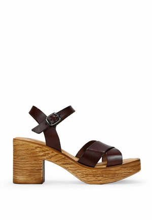 Sandalias de plataforma de cuero marrón con tiras entrelazadas y una correa en el tobillo ajustable, que cuentan con un tacón de bloque con textura de vetas de madera.