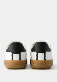 Witte sneakers met zwarte hielaccenten, voorzien van textuurleer en een gum rubberen zool. Opvallende decoratieve stiksels aan de achterkant.
