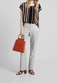 Top a strisce nera, rosa e marrone a maniche corte, pantaloni grigi sartoriali, borsa arancione con manico in tartaruga e sandali con tacco a blocco marroni.