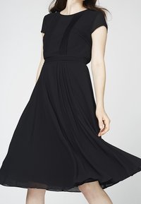 Schwarzes Kleid mit kurzen Ärmeln, gefälteltem Oberteil und schwingendem Rock. Hergestellt aus leichtem Stoff mit glatter Textur.