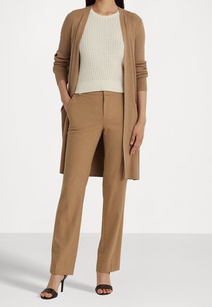 Femme portant un pantalon droit beige, un top blanc côtelé sans manches, un long cardigan beige et des sandales à talons noires.