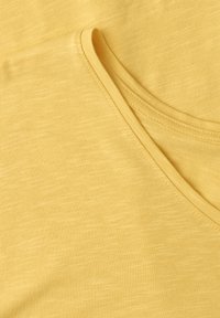Tissu en coton jaune avec un gros plan sur une couture courbe et une texture lisse, montrant de fins détails de tricot.