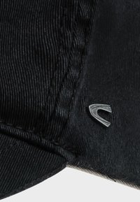 Zwarte corduroy pet met een gestructureerd oppervlak, voorzien van een klein zilveren logo accent aan de zijkant en een gebogen rand.