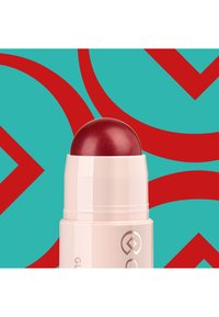 Un bâton de rouge à lèvres rouge avec un sommet arrondi, logé dans un contenant rose pâle. L'arrière-plan présente un bleu sarcelle avec des formes courbes rouges.