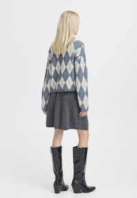 Maglione corto a fantasia diamante grigio e blu, gonna grigia e stivali neri a ginocchio con tacco. Tessuto a maglia morbido e silhouette aderente.