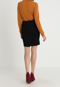 Černá sukně s přiléhavým střihem, doplněná zlatým topem s dlouhým rukávem s třpytivým efektem. Model má na sobě vínové kotníkové boty s texturovaným povrchem.
