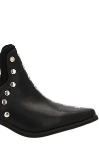 Botín de cuero negro hasta el tobillo con punta afilada, detalles de tachuelas plateadas a lo largo de los laterales y paneles elásticos en los costados para facilitar su uso. Diseño de suela plana.