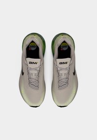 Αθλητικά παπούτσια ανοιχτού γκρι χρώματος με επάνω μέρος από δίχτυ, υφασμένο σχέδιο, αντανακλαστικές λεπτομέρειες και πράσινη διαφανής φτέρνα. Διαθέτουν μαύρο λογότυπο και κορδόνια.