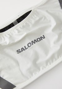 Weißer Stoff mit grauem "SALOMON"-Logo, ausgestattet mit elastischen und genähten Details, vermutlich Teil eines Sport- oder Outdoor-Zubehörs.