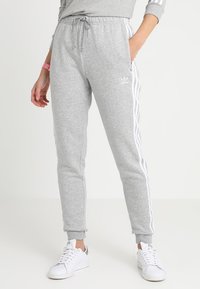 Pantalons de survêtement gris en mélange de coton ; avec des rayures blanches sur les côtés et une taille élastique. Assortis à des baskets blanches.