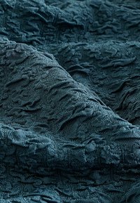 Tissu bleu sarcelle foncé avec des motifs texturés complexes en relief et des plis créant une surface douce et tactile.