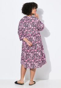 Rosa und schwarze Leopardenmuster-Kleid mit Dreiviertelärmel, gestuftem Design und lockerer Passform. Modell trägt schwarze Rutschsandaletten.