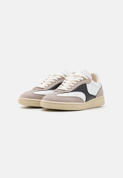 Sneakers with a suede upper in light gray and cream, accented by black leather details. Rubber sole with a textured finish. White laces.
