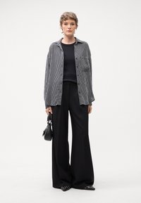 Pantaloni neri a gamba larga abbinati a un top nero e una camicia a righe grigia con bottoni. L'outfit include una piccola borsa nera e scarpe con punta.
