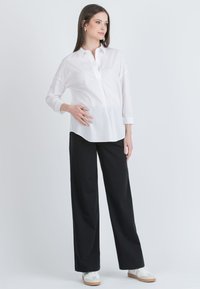 Bílá košile s dlouhými rukávy, doplněná černými širokými kalhotami a bílými teniskami. Košile má uvolněný střih a zakulacený lem.