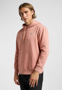 Felpa rosa realizzata in morbido tessuto, con tasca frontale, cappuccio con cordino e un piccolo logo blu "Lee" sul petto. Texture liscia.