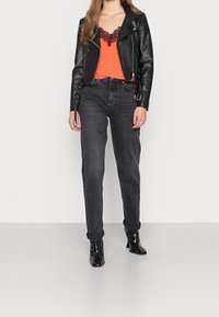 Zwarte leren motorjack over een oranje topje met kanten randje, gecombineerd met zwart, hooggetailleerde jeans en zwarte lakleren enkellaarsjes.