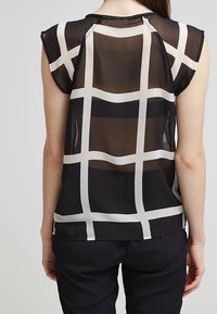 Svart genomskinlig blus med vitt rutmönster, korta ärmar och rund halsringning, med subtil textur och rena avslutningsdetaljer.
