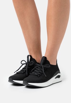 Black knit sneakers with a stretchy upper, black and silver speckled laces, and a white rubber sole featuring a textured design.