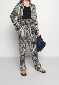 Pruhovaný kostým skládající se z přizpůsobeného blejzru a kalhot s širokými nohavicemi v krémové a námořnické barvě. Materiál má strukturovaný, abstraktní vzor a uvolněný střih.