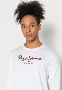 Langærmet hvid T-shirt med "Pepe Jeans London" i rød kursiv skrift, med klassisk rund hals og blødt bomuldsstof.