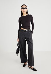 Top lung cu mâneci lungi de culoare neagră, pantaloni largi cu dungi subțiri gri, curea neagră cu cataramă argintie, ochelari de soare negri și pantofi cu vârf ascuțit de culoare neagră.